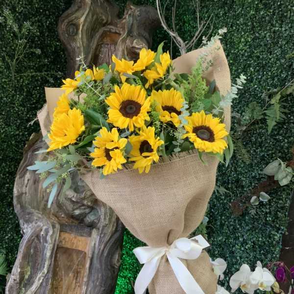 Bouquet of yellow sunflowers wrapped in burlap with a white ribbon