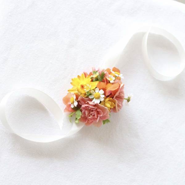 Small floral wrist corsage with pink, yellow, and orange blooms on a white ribbon