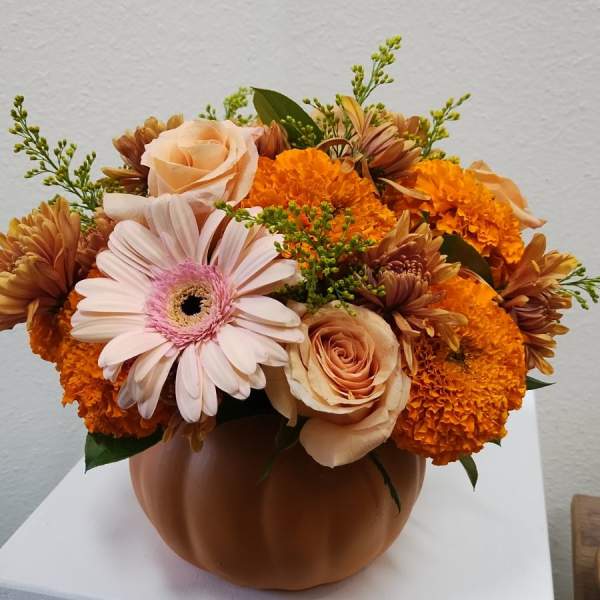 Orange and peach flowers arranged in a pumpkin-shaped vase