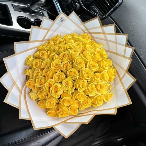 Large bouquet of yellow roses wrapped in white paper with gold trim