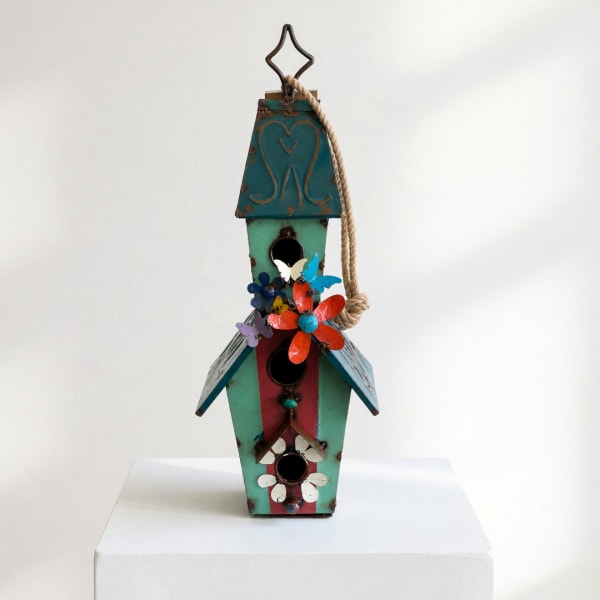 Decorative multicolored birdhouse with flower accents on a white pedestal