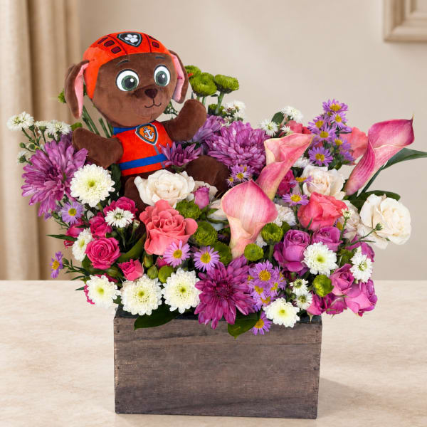 Stuffed dog in a flower arrangement with pink and white blooms in a wooden box