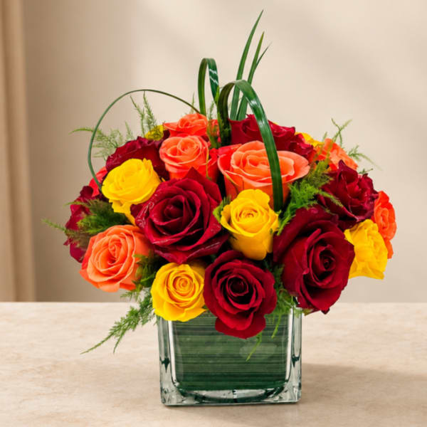 Bouquet of red, yellow, and orange roses in a square glass vase