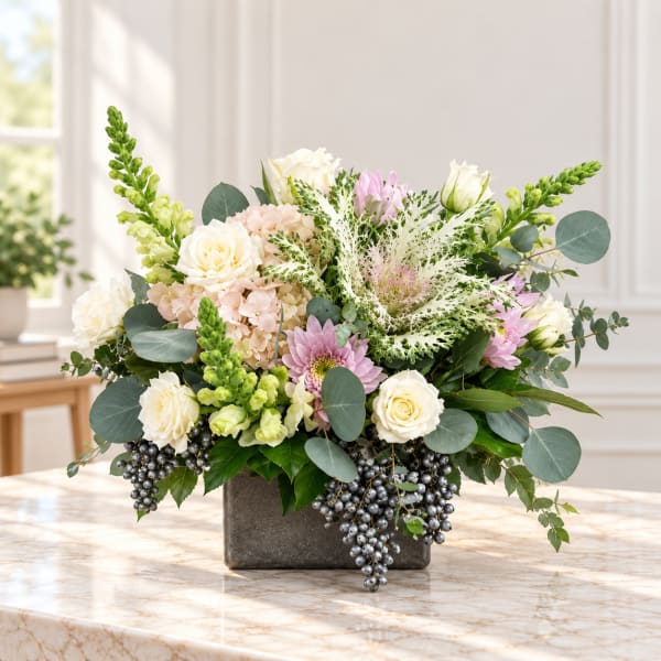 Mixed floral arrangement in a square gray vase with cream, pink, and green blooms