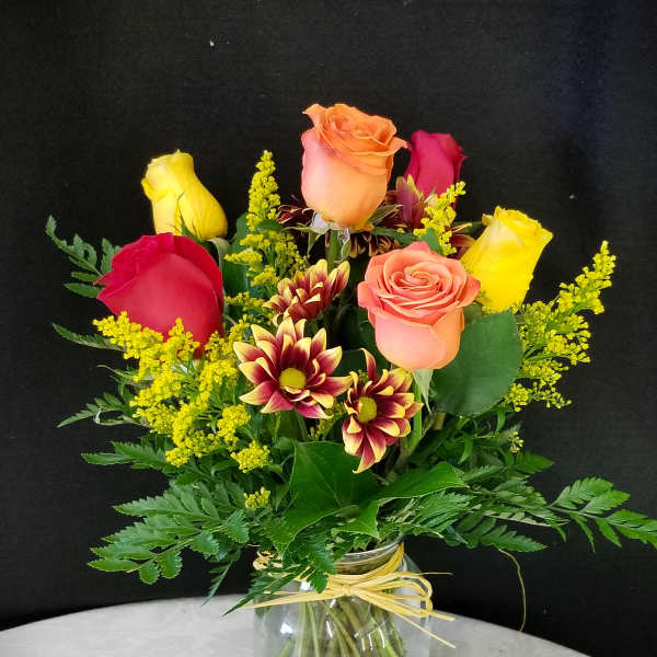 Mixed roses and chrysanthemums in a glass vase with yellow filler flowers