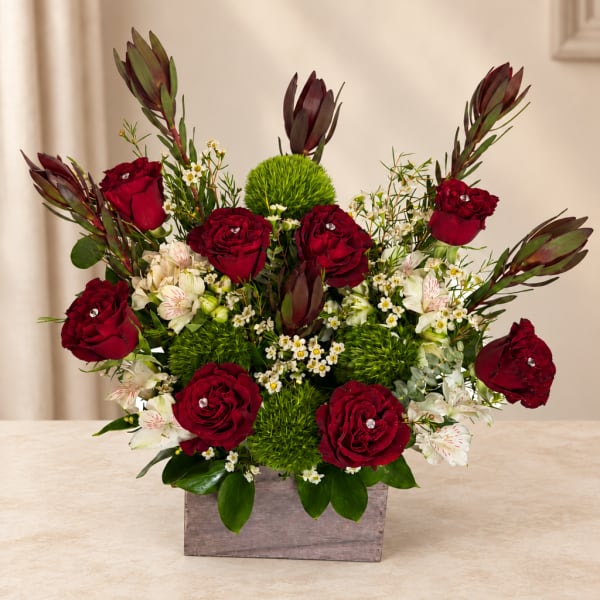 Red roses and white flowers arranged in a wooden box with green accents