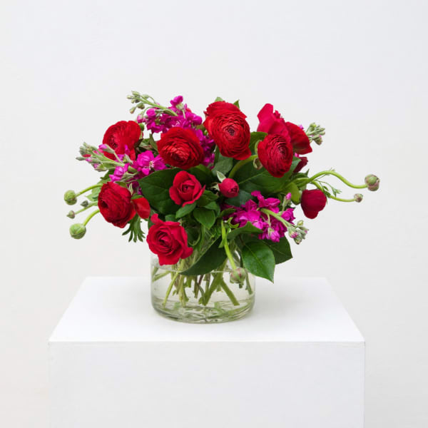 Red roses and magenta flowers arranged in a clear glass vase