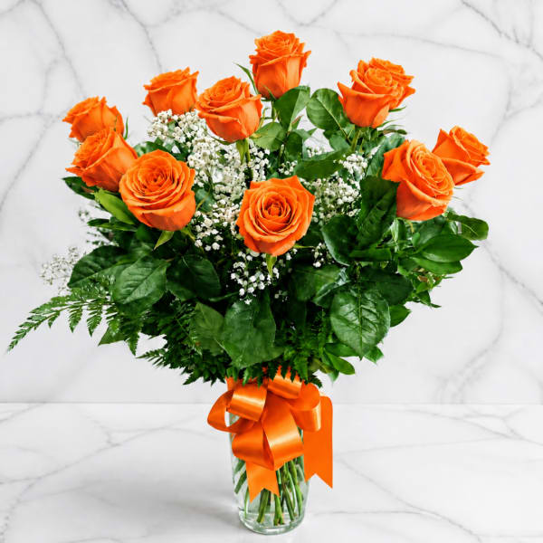 Orange roses in a clear glass vase with a ribbon bow
