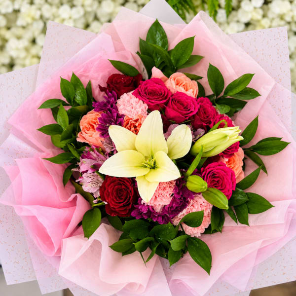 Pink bouquet with roses, carnations, and a white lily wrapped in pink paper