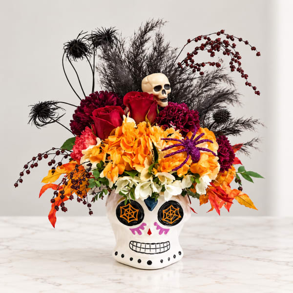 Halloween floral arrangement in a painted skull vase with red, orange, and purple flowers