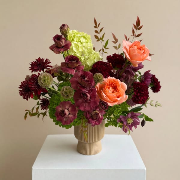 Mixed floral arrangement in a ribbed beige vase with peach and burgundy blooms