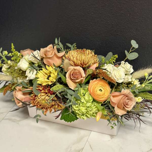Low floral arrangement with peach roses, white blooms, and yellow chrysanthemums in a white box.