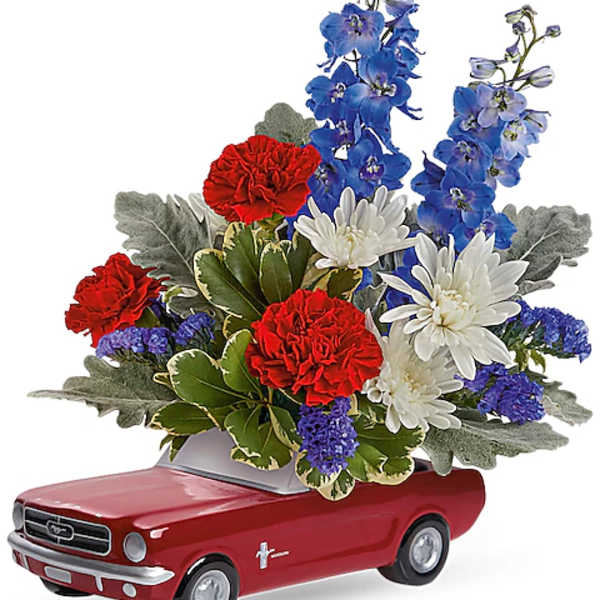 Flower arrangement in a red toy car planter with red, white, and blue blooms