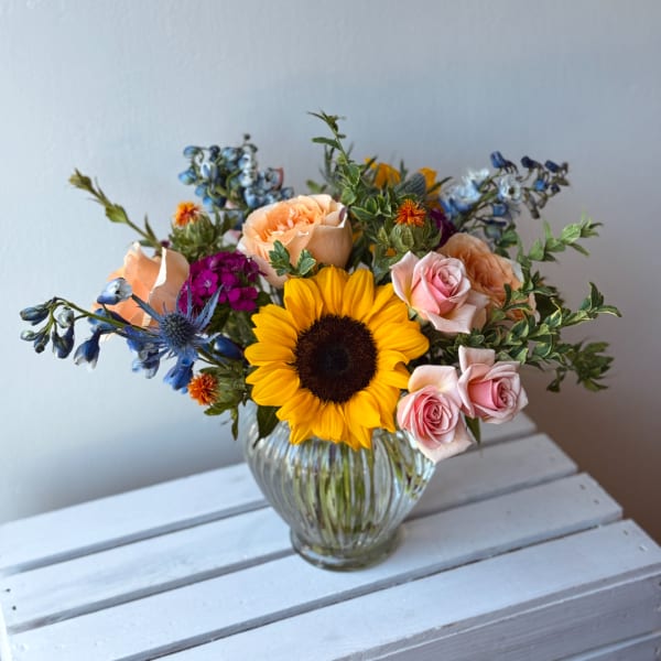 Mixed bouquet with a sunflower, pink roses, and blue flowers in a glass vase