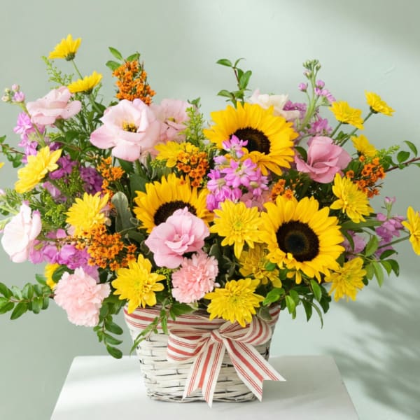 Basket arrangement with sunflowers, pink blooms, and a striped ribbon