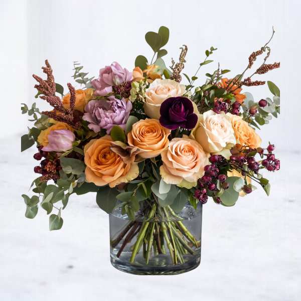 Mixed rose bouquet in a clear glass vase with peach, cream, purple, and orange blooms