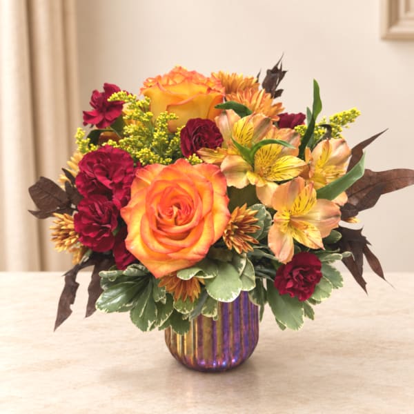 Orange and burgundy floral arrangement in a ribbed iridescent vase