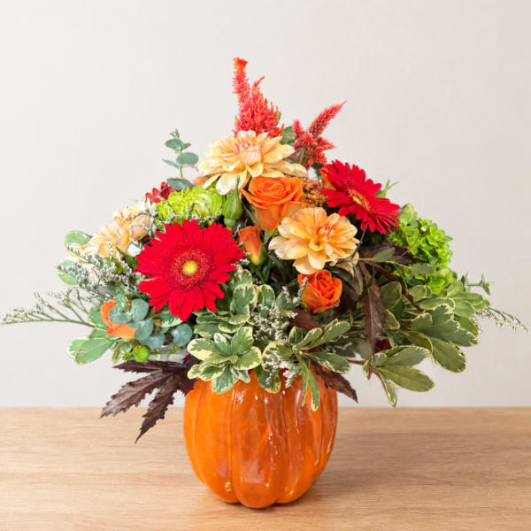 Orange pumpkin vase with red and orange flowers and mixed greenery