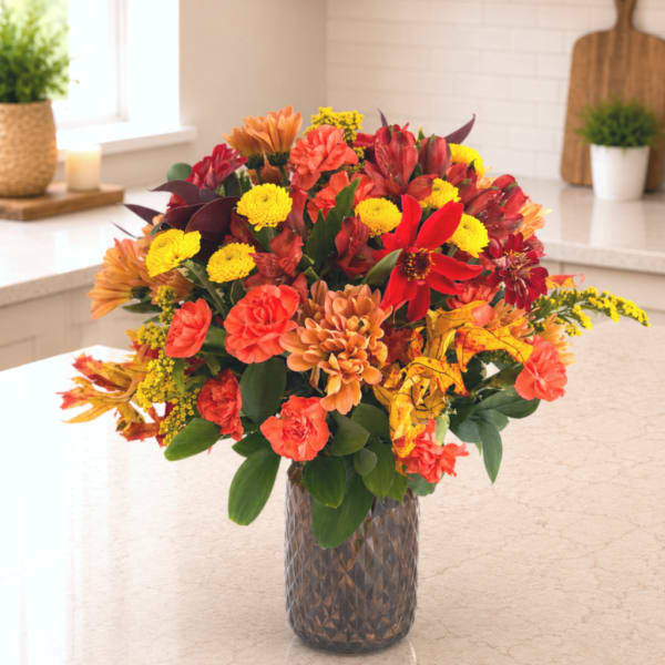 Mixed autumn bouquet in a textured glass vase with red, orange, and yellow blooms