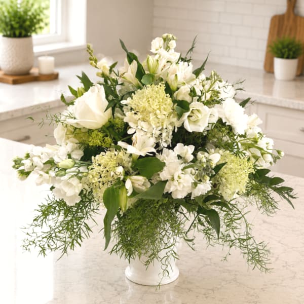 White floral arrangement in a white vase with trailing greenery