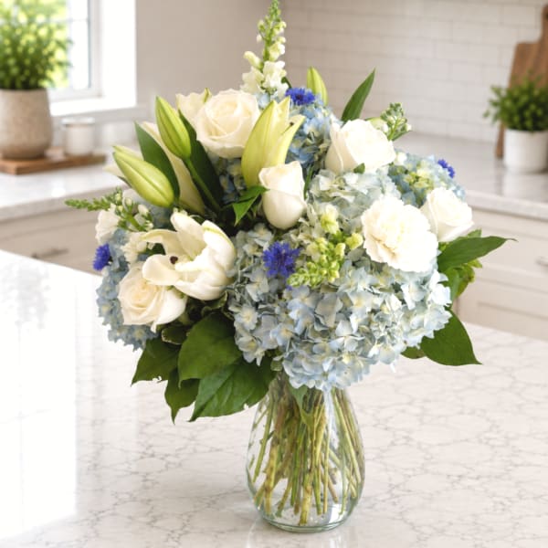 White roses and lilies with blue hydrangeas in a glass vase
