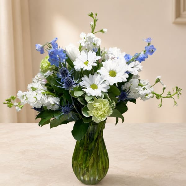 White and blue mixed flowers arranged in a green glass vase