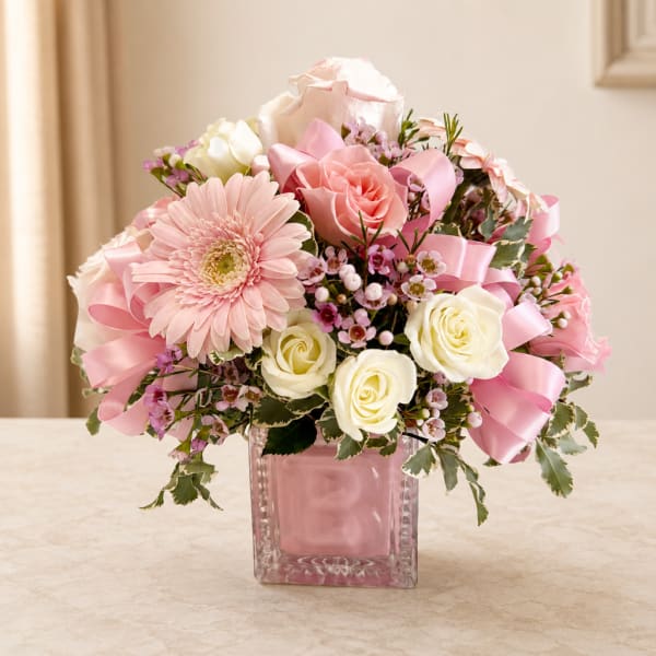 Pink and white flower arrangement in a square glass vase with ribbon