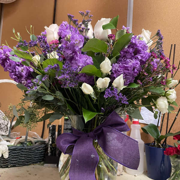 Purple and white flower bouquet in a clear glass vase with a purple ribbon