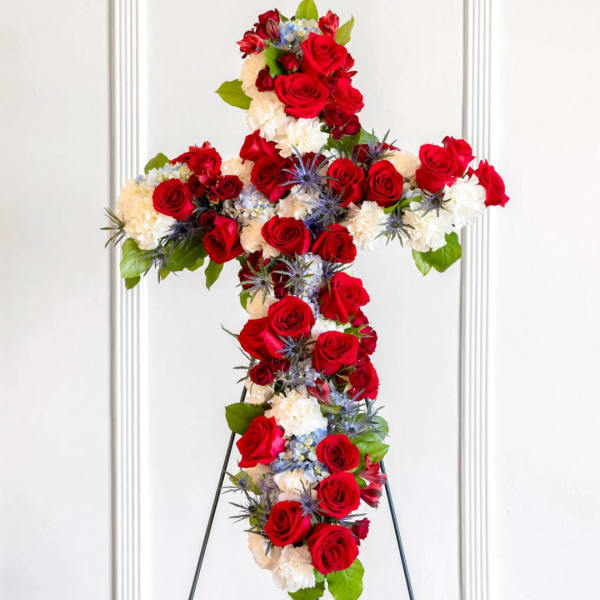Floral cross arrangement with red roses, white carnations, and blue accents