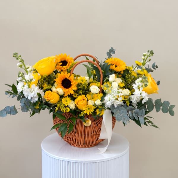 Yellow and white flower arrangement in a wicker basket with ribbon