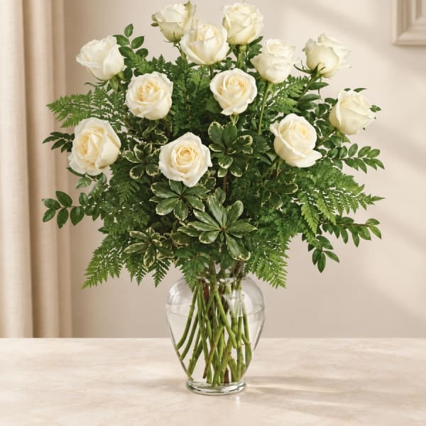 White roses arranged in a clear glass vase with lush greenery