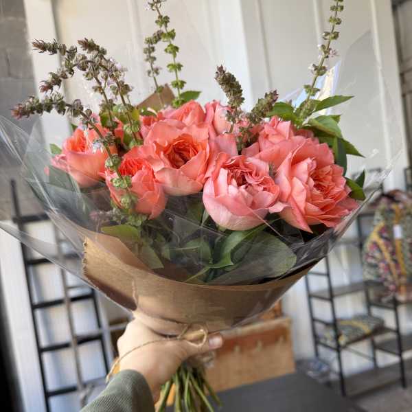 Handheld bouquet of pink roses wrapped in brown paper and clear plastic
