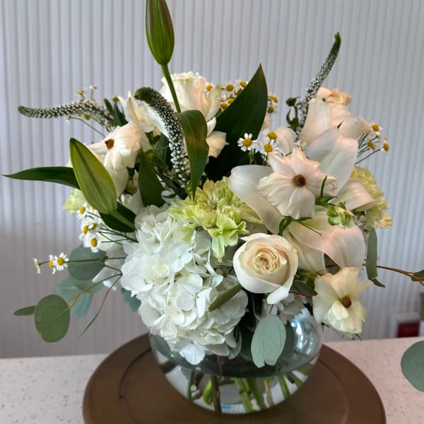 White floral arrangement in a glass vase with lilies, roses, and hydrangeas