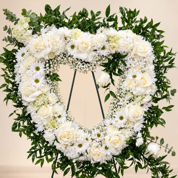 Heart-shaped white floral wreath on a stand with roses and daisies