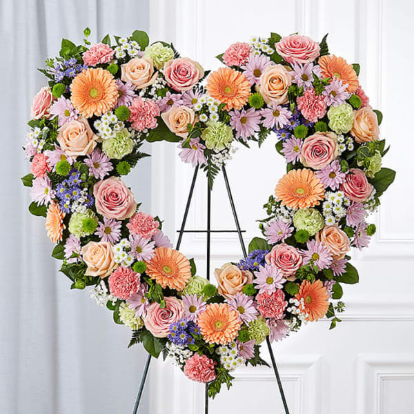 Heart-shaped floral wreath on a stand with pink, peach, and orange blooms