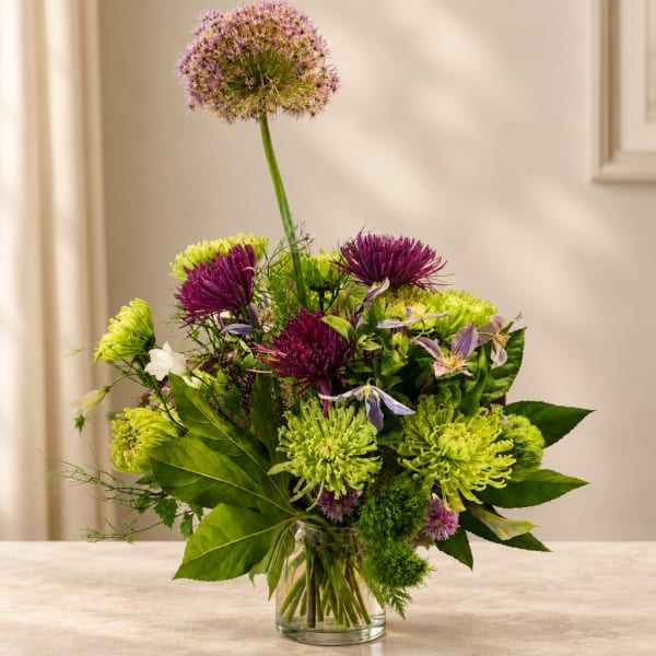 Purple and green mixed bouquet in a clear glass vase