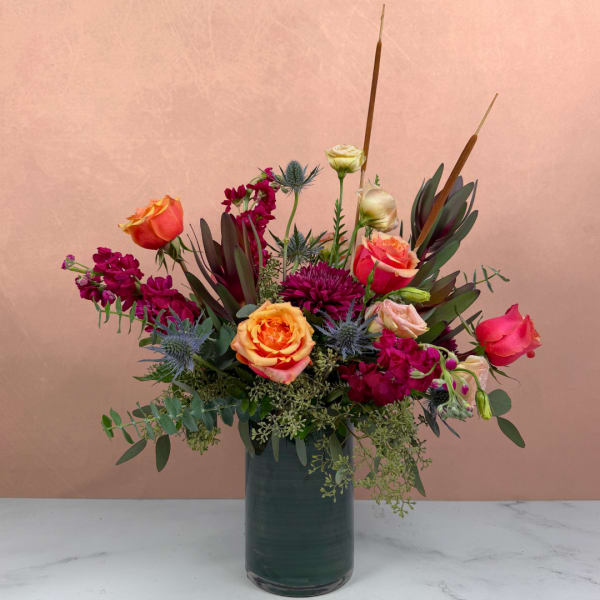 Mixed bouquet of orange and pink roses in a dark glass vase
