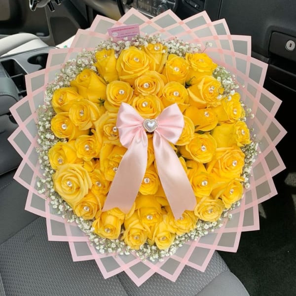 Yellow rose bouquet with a pink ribbon and clear wrap in a car seat