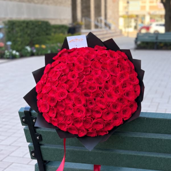 Large bouquet of red roses wrapped in black paper on a bench