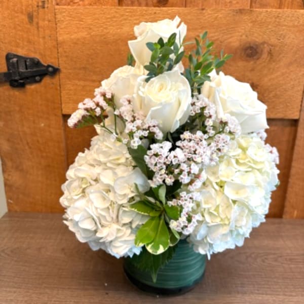 White roses and hydrangeas in a green vase with small pink filler flowers