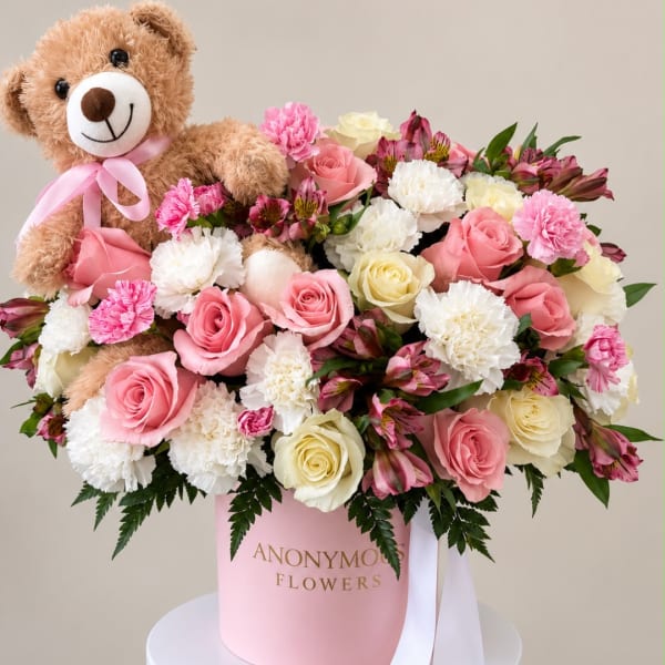 Pink and white flower arrangement with a teddy bear in a pink box