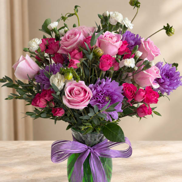 Pink and purple bouquet of roses and carnations in a glass vase with a purple ribbon