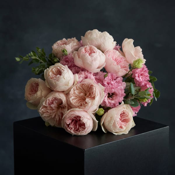 Blush pink and cream bouquet of peonies and carnations on a black pedestal