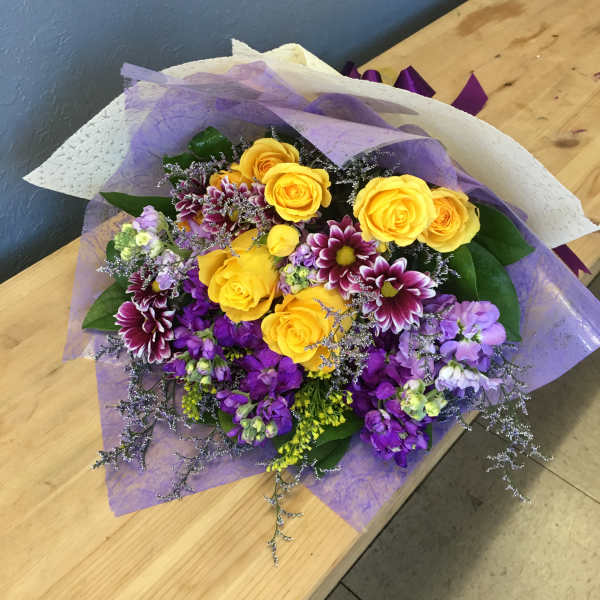 Bouquet of yellow roses and purple flowers wrapped in lavender paper