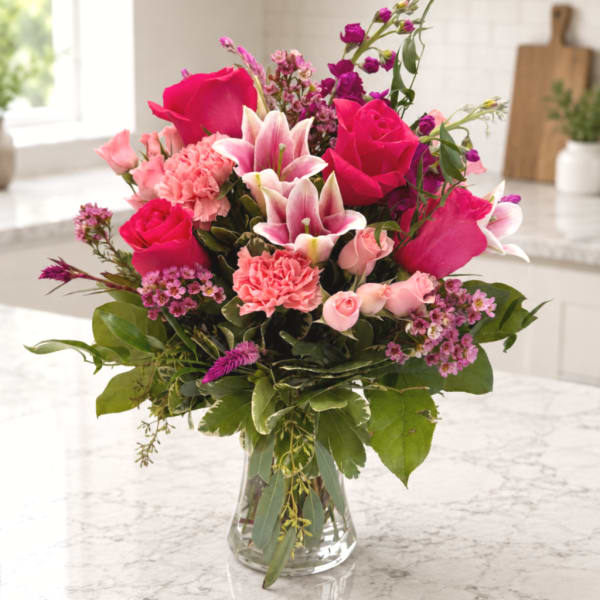 Pink roses, lilies, and carnations in a clear glass vase