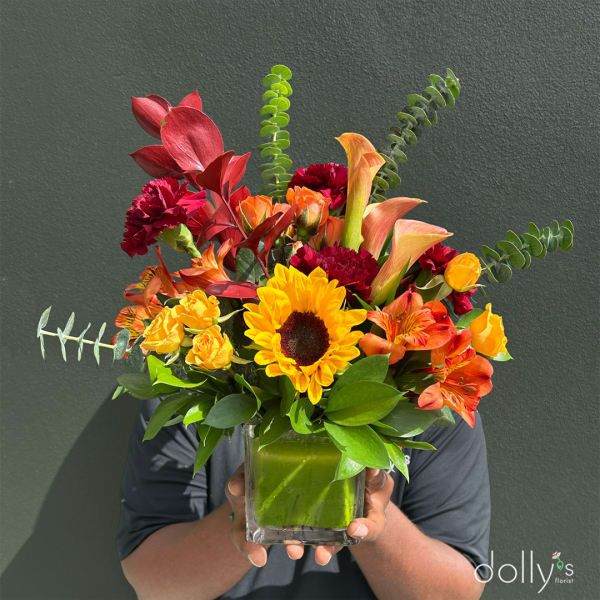 Bright mixed bouquet in a square glass vase with a sunflower and orange blooms