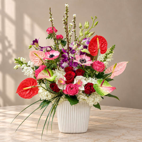 Colorful floral arrangement in a white ribbed vase with roses and orchids