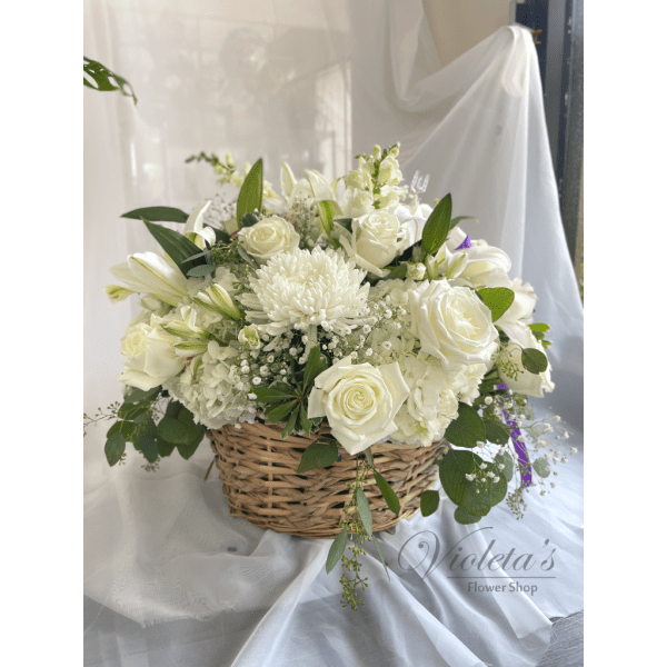 White floral arrangement in a wicker basket with roses and lilies