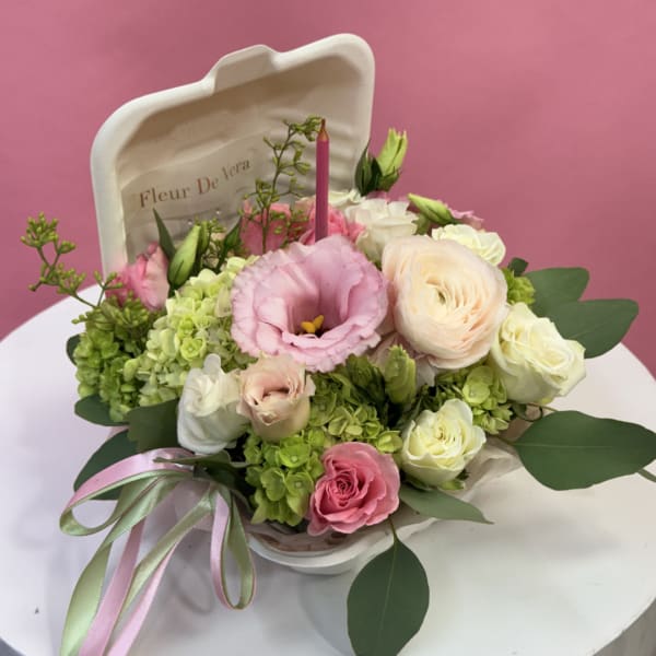 Pink and cream floral arrangement in a white container with ribbon