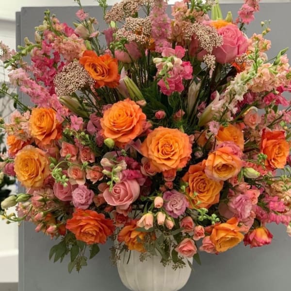 Large wedding arrangement of orange and pink roses in a white vase